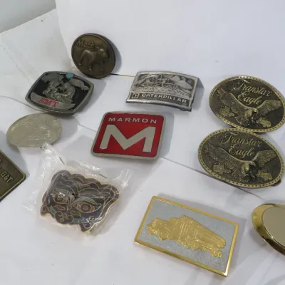 Collection of vintage belt buckles featuring various themes, including Caterpillar, Marmon, Transtar Eagle, and Mack Trucks.
