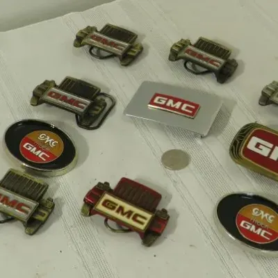Collection of vintage GMC belt buckles in various styles, including truck grille designs and oval logos.
