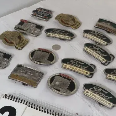 Collection of vintage metal belt buckles featuring Ford Trucks, Caterpillar, and other automotive themes.