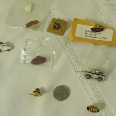 Collection of vintage REO Motor Car Company and related advertising lapel pins, some in original packaging, shown with a U.S. quarter for...