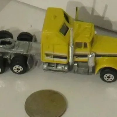 Vintage Matchbox Peterbilt conventional sleeper cab semi-truck in yellow, showing some paint wear, pictured next to a coin for scale.