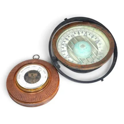 Sale Photo Thumbnail #191: Vintage maritime instruments including a gimbaled ship's compass with a brass bezel and a wall-mounted aneroid barometer in a carved wooden frame.