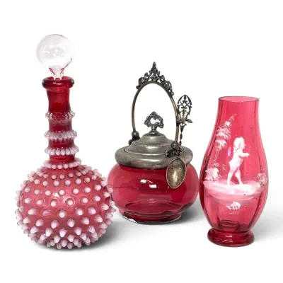 Sale Photo Thumbnail #211: Collection of antique cranberry glass items, including a Fenton hobnail decanter with stopper, a silver-plated lidded jam jar with spoon, and a Mary Gregory style enameled vase.