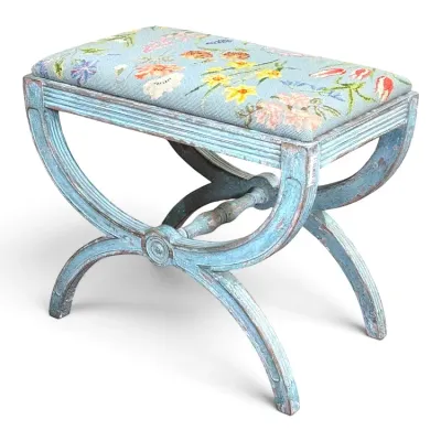 Sale Photo Thumbnail #85: Vintage French-style curule bench featuring a distressed light blue painted frame and a needlepoint upholstered seat with a floral motif.