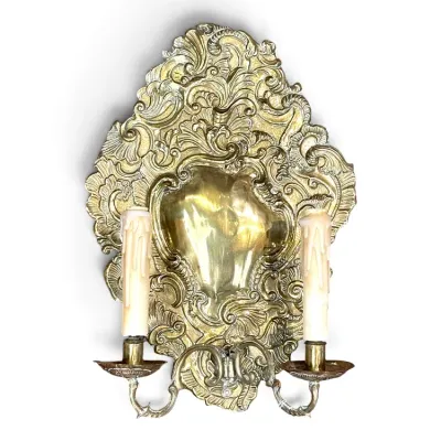 Sale Photo Thumbnail #185: Ornate Rococo-style brass wall sconce featuring a heavily detailed backplate with scrollwork and two candle-style lights with faux-drip covers.