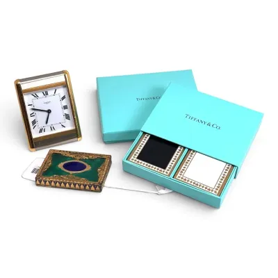 Sale Photo Thumbnail #138: Luxury desk accessories including a Cartier travel clock, an ornate green and gold enamel compact, and a Tiffany & Co. double deck playing card set in its original blue box.