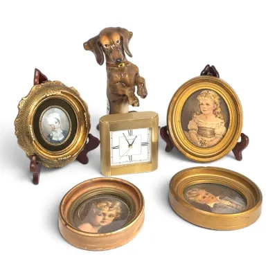 Sale Photo Thumbnail #206: Collection of vintage tabletop items, including four small framed portraits in ornate gold-toned frames, a Tiffany & Co. brass desk clock, and a ceramic dachshund figurine.