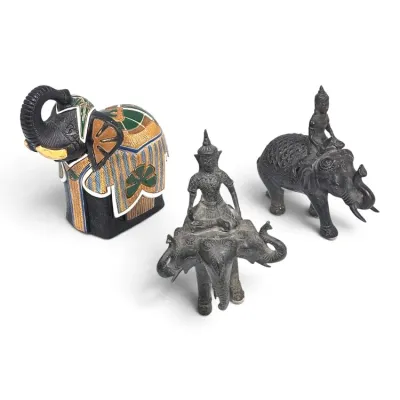 Sale Photo Thumbnail #193: Three decorative elephant figurines, including a colorful ceramic elephant with a patterned blanket and two dark metal figurines depicting riders atop elephants.