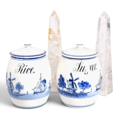 Sale Photo Thumbnail #205: Pair of vintage Delft-style blue and white ceramic canisters labeled for rice and sugar, flanked by two clear quartz crystal obelisks.