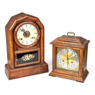 Sale Photo Thumbnail #197: Two vintage wooden mantel clocks, including an antique steeple-style clock with a floral painted glass panel and a Howard Miller bracket-style clock with a brass carrying handle.