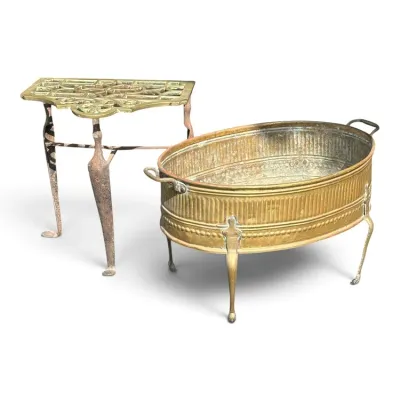 Sale Photo Thumbnail #235: Antique brass fireplace trivet with a pierced top and three legs, paired with a vintage brass coal scuttle or log holder featuring a ribbed body and paw feet.
