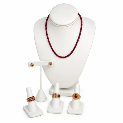 Sale Photo Thumbnail #5: Collection of ruby and gold jewelry, including a beaded necklace, stud earrings, and three distinct gold rings set with rubies, displayed on white stands.