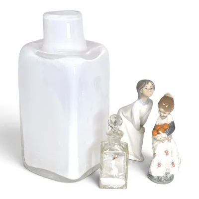 Sale Photo Thumbnail #219: Collection of decorative items featuring a large white cased glass vase, a small etched glass perfume bottle with a faceted stopper, and two Lladró-style porcelain figurines of young girls.