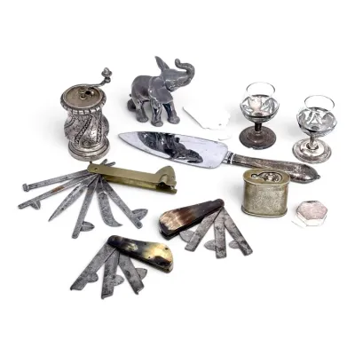 Sale Photo Thumbnail #137: Assortment of vintage metalware and medical tools, including a silver-plated cake server, small goblets, an elephant figurine, a pepper grinder, and several antique fleams with horn and brass handles.