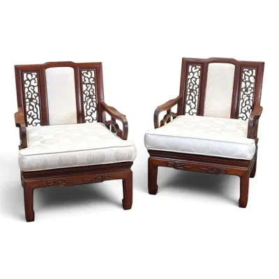 Sale Photo Thumbnail #113: Pair of Chinese-style carved hardwood armchairs featuring intricate openwork back panels, key fret apron details, and upholstered white cushions with a subtle circular pattern.