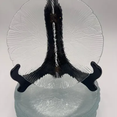 Sale Photo Thumbnail #95: Set of vintage textured clear glass plates featuring a scalloped edge and a radiating leaf pattern, displayed on a black stand.