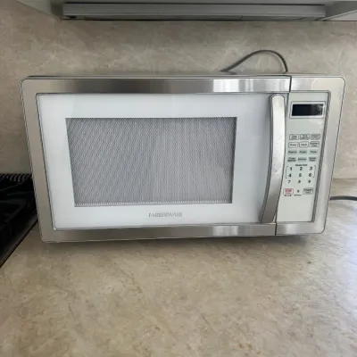 Sale Photo Thumbnail #21: Farberware countertop microwave oven featuring a stainless steel and white finish with a digital control panel.