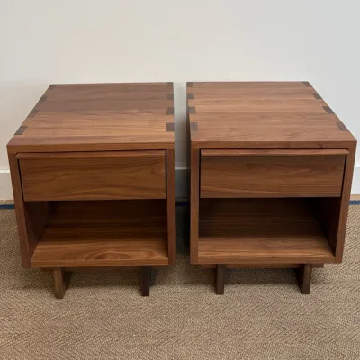 Sale Photo Thumbnail #30: Pair of modern walnut nightstands featuring exposed joinery on the top surface, a single drawer, and an open lower shelf.