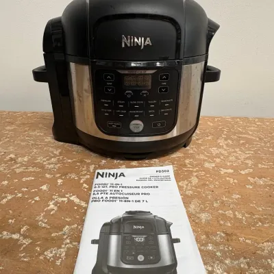 Sale Photo Thumbnail #150: Ninja Foodi 11-in-1 6.5-quart Pro Pressure Cooker, model FD302, in black and stainless steel finish, complete with its original owner's guide.