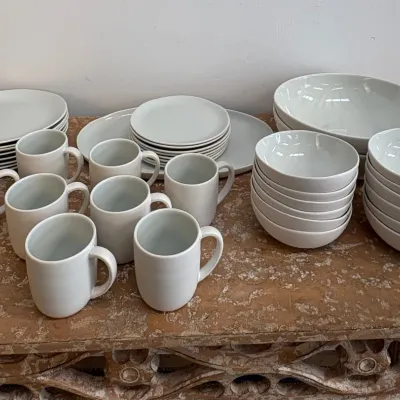 Sale Photo Thumbnail #122: Minimalist white ceramic dinnerware set, including plates, bowls, and mugs, displayed on a rustic wooden table.