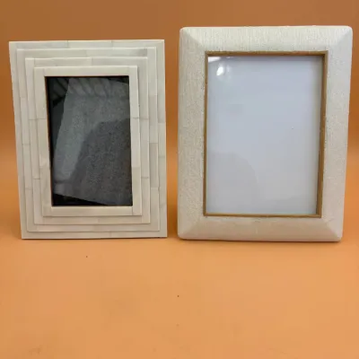 Sale Photo Thumbnail #64: Two decorative tabletop picture frames, including a white bone inlay frame with a tiered design and a textured cream fabric frame with gold trim.