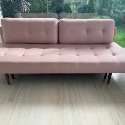 Sale Photo Thumbnail #18: Mid-century modern style futon sofa in dusty pink upholstery, featuring a tufted seat, two matching back cushions, and tapered wooden legs.