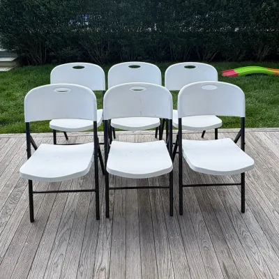 Sale Photo Thumbnail #26: Set of six white plastic folding chairs with black metal frames, showing some light wear from outdoor use.