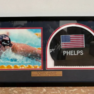 Sale Photo Thumbnail #105: Framed Michael Phelps memorabilia display featuring an autographed swim cap and a photo from the 2008 Beijing Olympics, complete with a commemorative plaque.