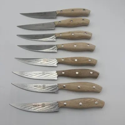 Sale Photo Thumbnail #104: Set of eight Schmidt Brothers steak knives featuring Damascus-style steel blades and light wood handles with triple-rivet construction.