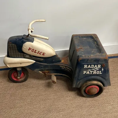 Sale Photo Thumbnail #170: Vintage Murray "Radar Patrol" chain-drive police tricycle, featuring a blue and white metal body with original decals, showing some rust and wear consistent with age.