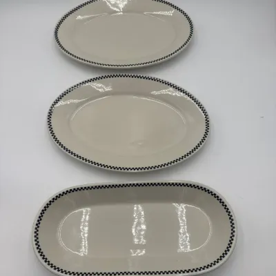 Sale Photo Thumbnail #56: Three vintage ceramic serving platters featuring a cream glaze and a black-and-white checkered border, including two oval platters and one elongated oblong dish.