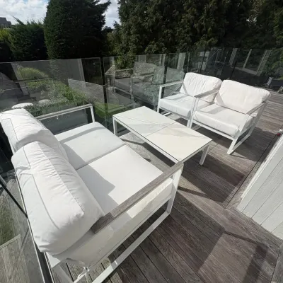 Sale Photo Thumbnail #6: Modern outdoor patio set featuring a white metal frame loveseat, two matching armchairs with white cushions, and a rectangular coffee table with a light-colored top.