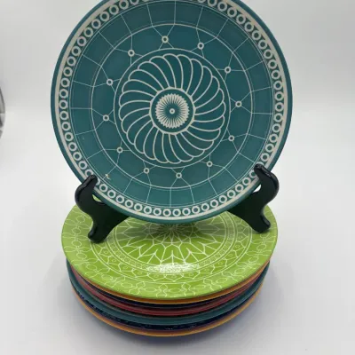 Sale Photo Thumbnail #112: Stack of colorful ceramic plates featuring intricate white geometric and floral patterns, with one teal plate displayed upright on a black stand.