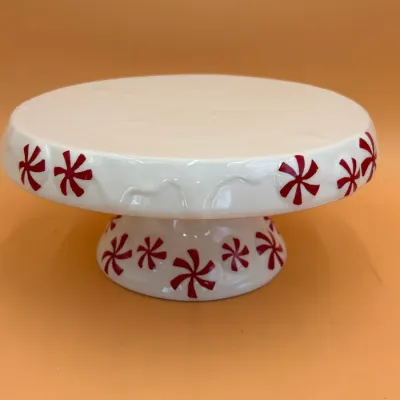 Sale Photo Thumbnail #69: Ceramic pedestal cake stand featuring a white glaze with red peppermint candy motifs and a dripping icing detail along the rim.