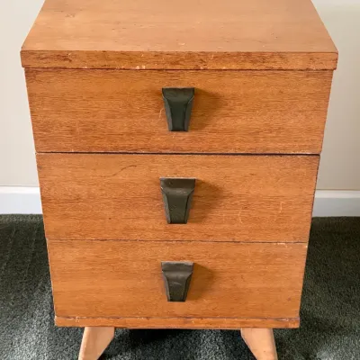 Sale Photo Thumbnail #54: Mid-century modern three-drawer nightstand with tapered wooden legs and unique dark metal pulls.