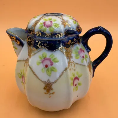 Sale Photo Thumbnail #63: Vintage Nippon-style porcelain lidded syrup pitcher or creamer, featuring hand-painted pink floral motifs, cobalt blue accents, and detailed gold moriage gilding.