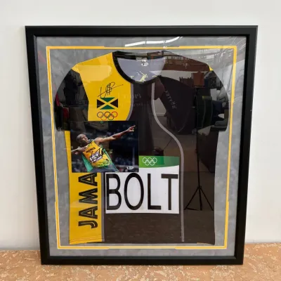 Sale Photo Thumbnail #103: Framed Usain Bolt memorabilia display featuring a signed Jamaican Olympic jersey, a signed photograph of his iconic pose, and a replica competitor bib.