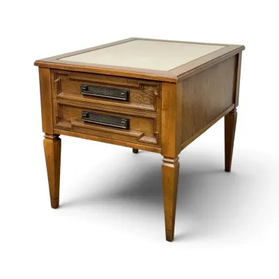 Sale Photo Thumbnail #133: Mid-century modern wooden end table featuring two drawers with textured metal pulls, tapered legs, and a light-colored laminate or leather-look top insert.