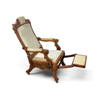 Sale Photo Thumbnail #148: Antique Victorian reclining Morris chair with carved wood frame, cream-colored patterned upholstery, and an integrated pull-out footrest.