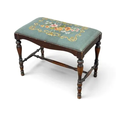 Sale Photo Thumbnail #152: Vintage wooden vanity bench featuring turned legs, an H-stretcher, and a needlepoint upholstered seat with a floral motif on a sage green background.
