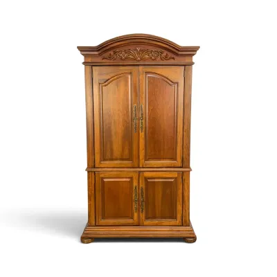 Sale Photo Thumbnail #68: Traditional wooden armoire featuring an arched crown with floral carvings, brass hardware, and a two-tiered cabinet design.