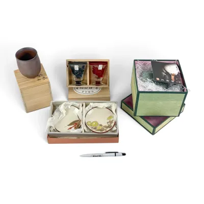 Sale Photo Thumbnail #45: Assortment of Japanese tableware and decorative items, including a ceramic cup with a wooden box, a pair of cut glass sake cups, small floral plates, and a boxed green ceramic vessel.