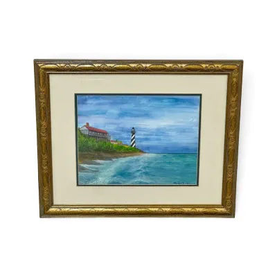 Sale Photo Thumbnail #320: Framed watercolor painting depicting a coastal scene with a spiral-striped lighthouse, signed and dated 1997, housed in an ornate gold-finished frame.