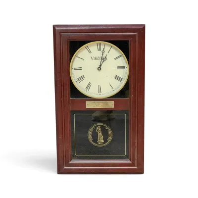 Sale Photo Thumbnail #315: University of Virginia wooden mantle clock featuring Roman numerals, a commemorative plaque, and the university seal on the lower glass panel.