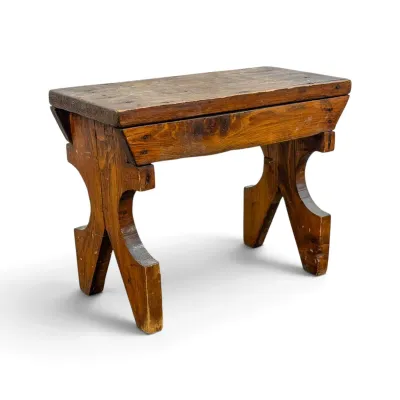 Sale Photo Thumbnail #277: Rustic handmade wooden bench or stool with a distressed finish and uniquely carved trestle-style legs.