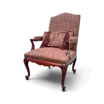 Sale Photo Thumbnail #178: Queen Anne style armchair featuring burgundy damask upholstery, brass nailhead trim, and carved cabriole legs, complete with a matching tasseled accent pillow.