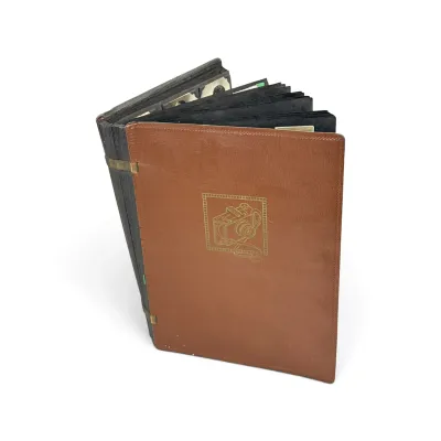 Sale Photo Thumbnail #40: Vintage photo album with a brown textured cover featuring a gold-embossed camera illustration, filled with black paper pages.