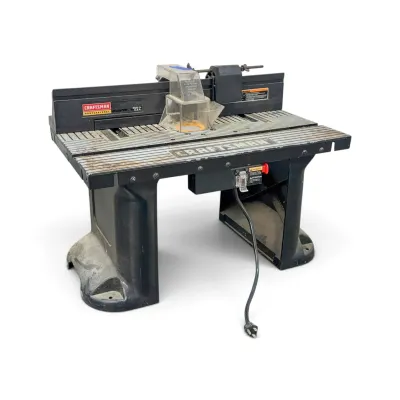 Sale Photo Thumbnail #238: Craftsman Professional router table featuring a ribbed aluminum top, adjustable fence, and clear safety guard, showing some wear from use.