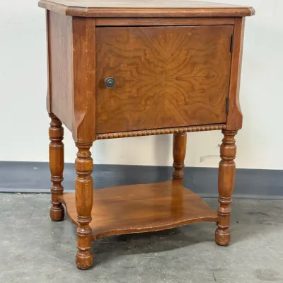 Sale Photo Thumbnail #177: Vintage wooden nightstand or side table featuring a single cabinet door with bookmatched veneer, turned legs, and a lower shelf.