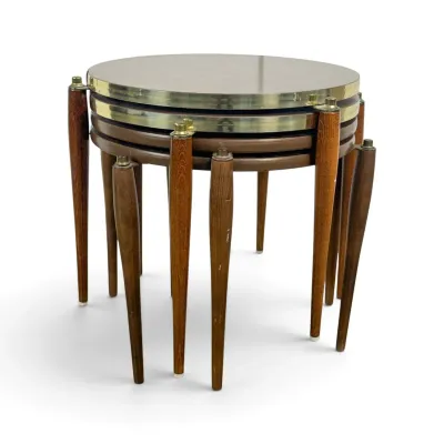 Sale Photo Thumbnail #100: Mid-century modern nesting tables featuring round laminate tops with brass-toned metal trim and tapered wooden legs.